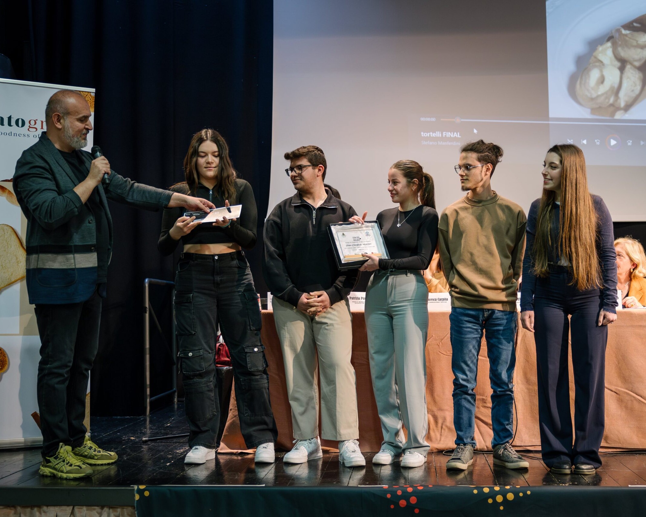 Un evento di premiazione con cinque giovani che ricevono un riconoscimento su un palco