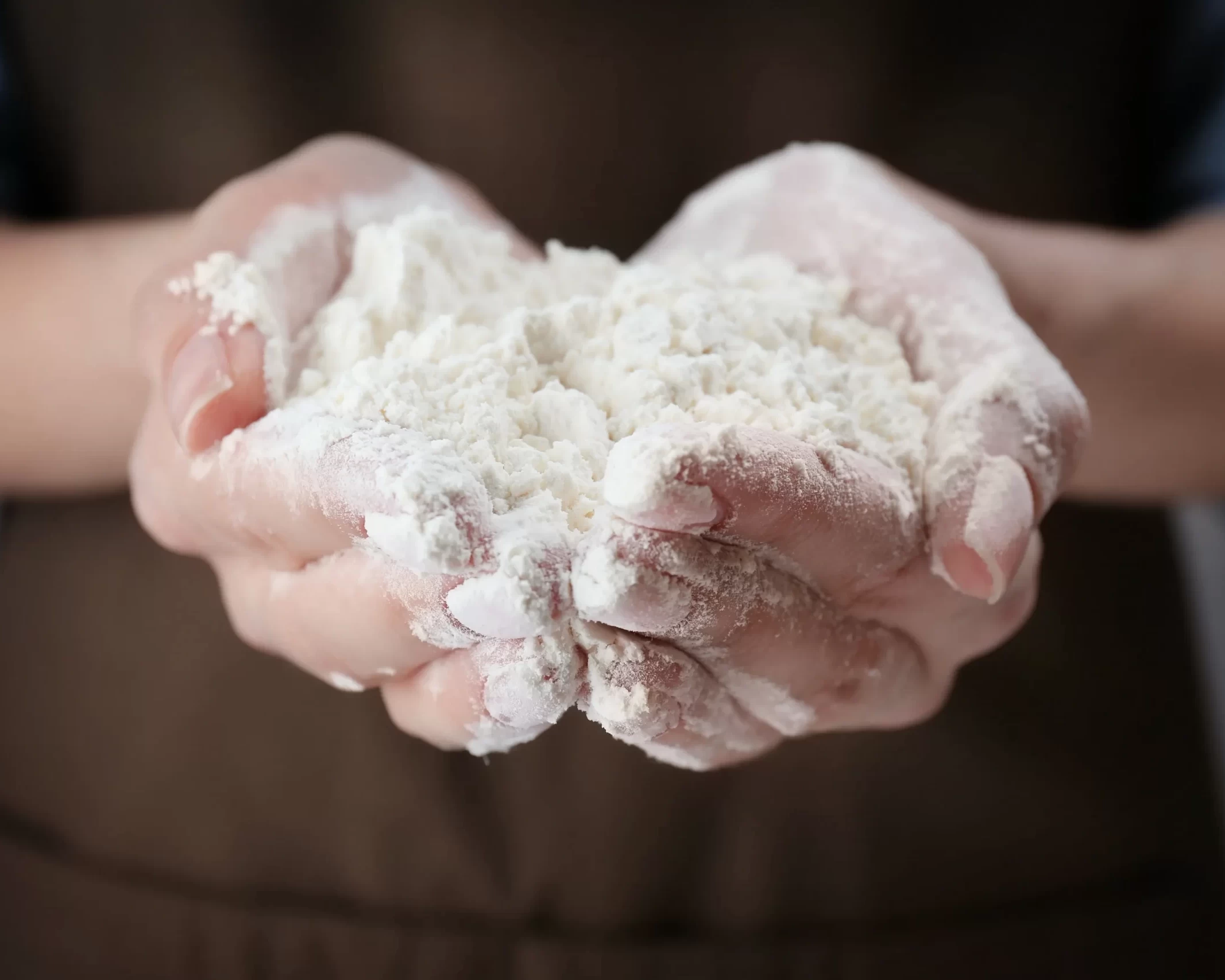 Persona che tiene una manciata di farina bianca fresca per la preparazione di dolci