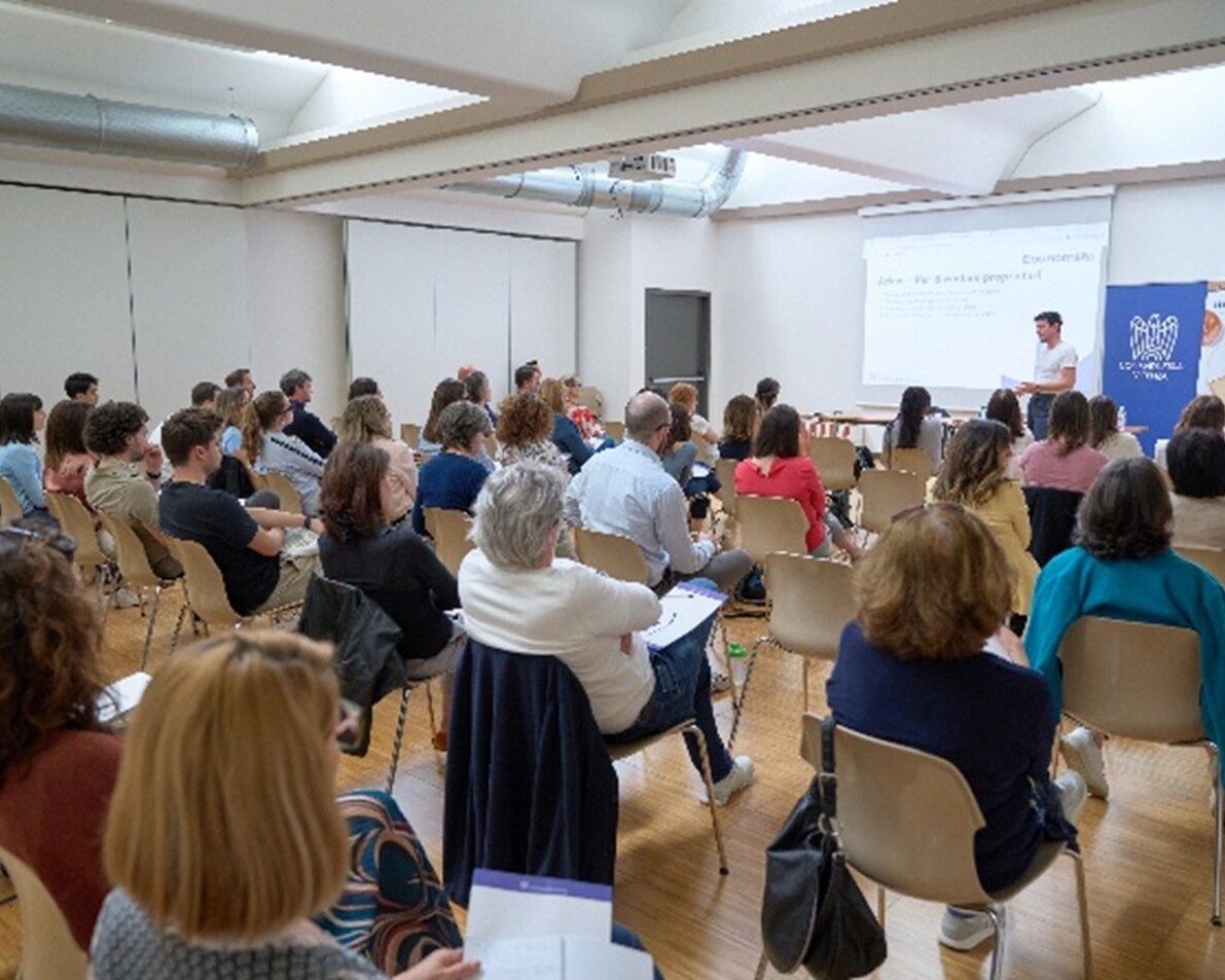 A packed hall during a seminar with participants listening to a speaker.