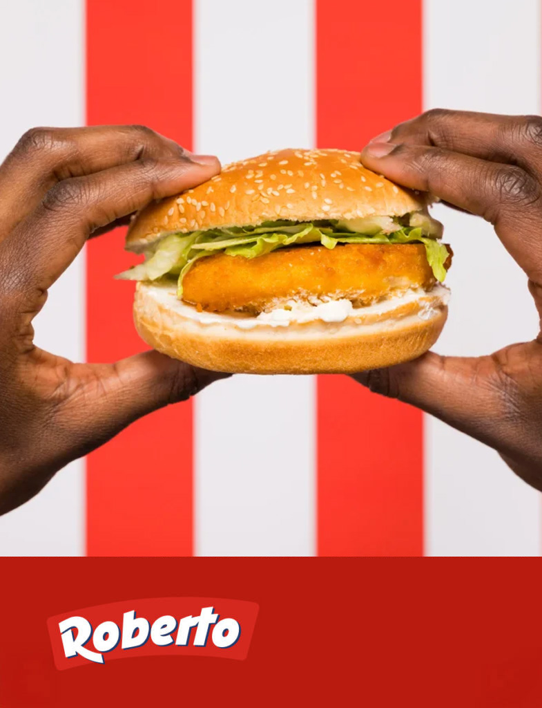 Un panino con pollo impanato e verdure tenuto da mani su sfondo a righe rosse e bianche