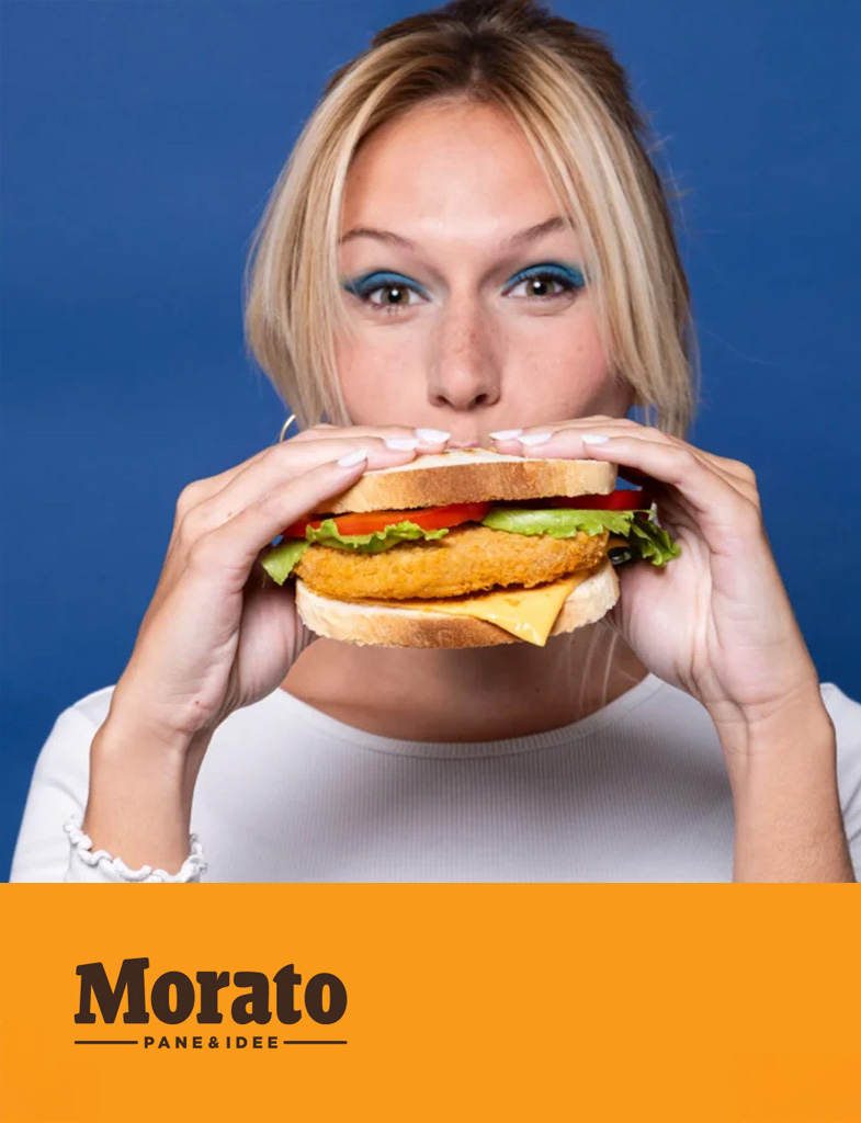Donna con trucco brillante che tiene un grande panino con lattuga, pomodoro e formaggio